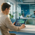 A young adult analyzes an e-commerce dashboard with an upward-trending graph on a tablet in a bright, modern office.