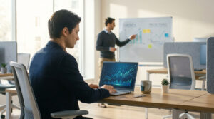 Homme travaillant sur un ordinateur portable avec des graphiques financiers. Un collègue présente des projections au tableau.